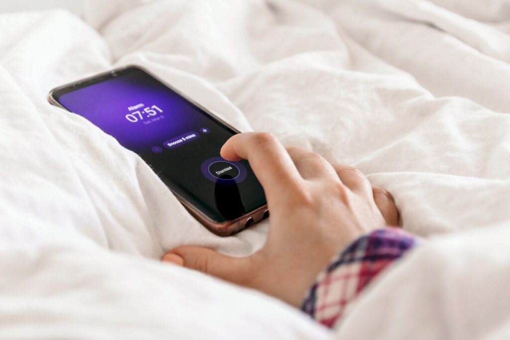 Close-up image of hand pressing dismiss button on alarm on mobile phone. Woman in bed, snooze, alarm clock, wake up, morning, early.