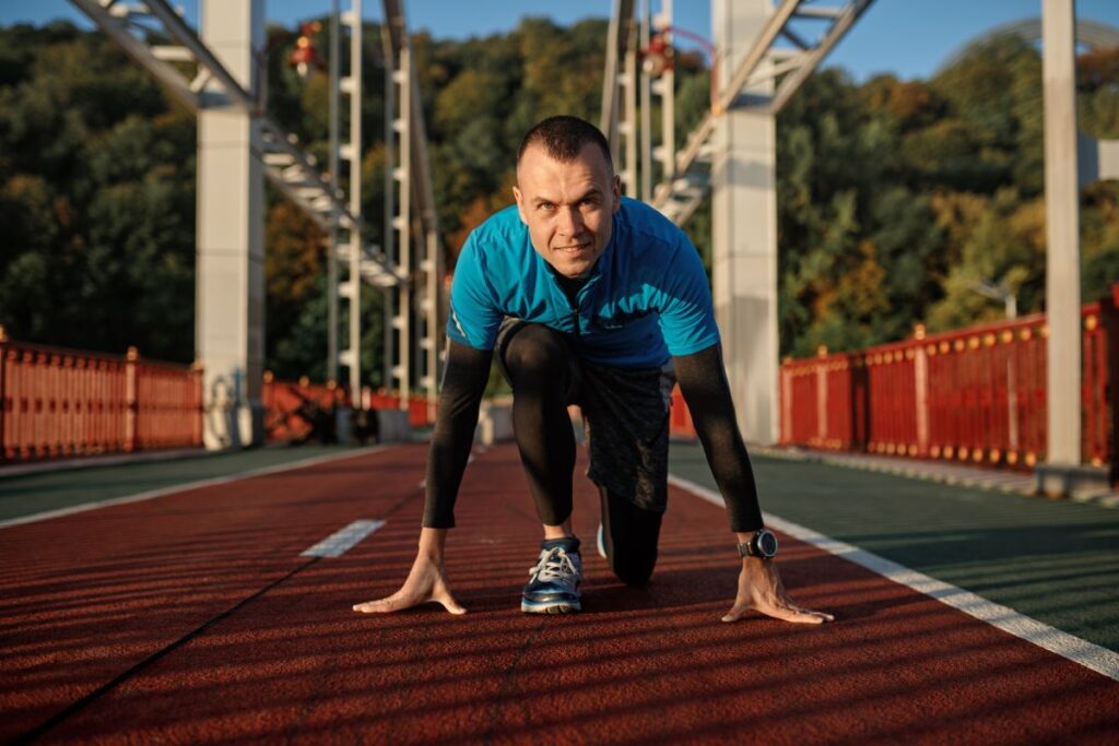 Portrait of adult speed runner in starting position ready for running on sports track