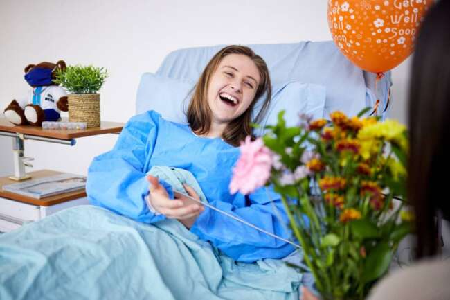 Sick, hospital patient and visitor with flowers at bed with a woman in recovery with support. Healt.
