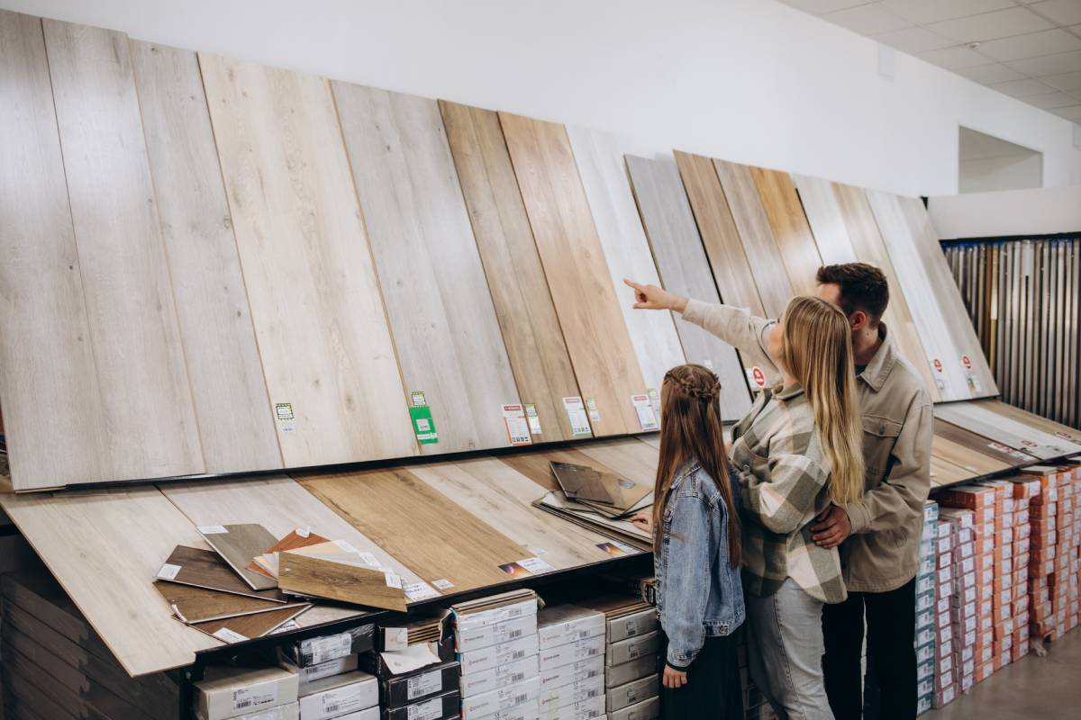 Modern family couple standing together with sample of laminated flooring in building store.