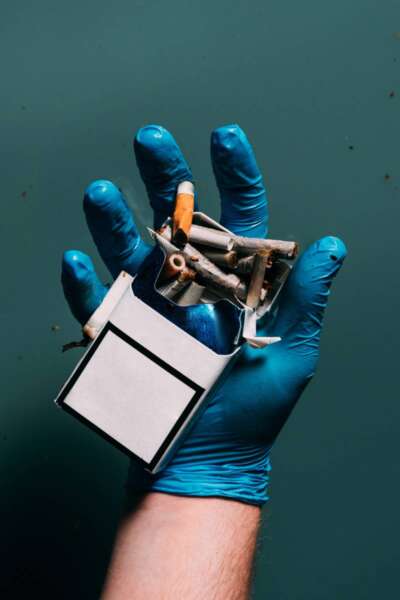 partial view of man in latex glove holding cigarettes in hand, ecosystem protection concept
