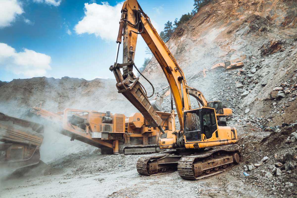 Industrial excavator loading ore and stone material from highway construction site into a dumper truck